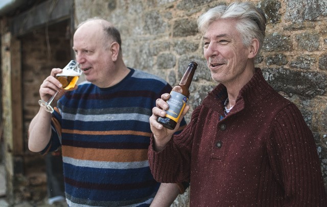 Barnaby and Tim from Barnaby's Brewhouse drinking beers in front of a stone wall